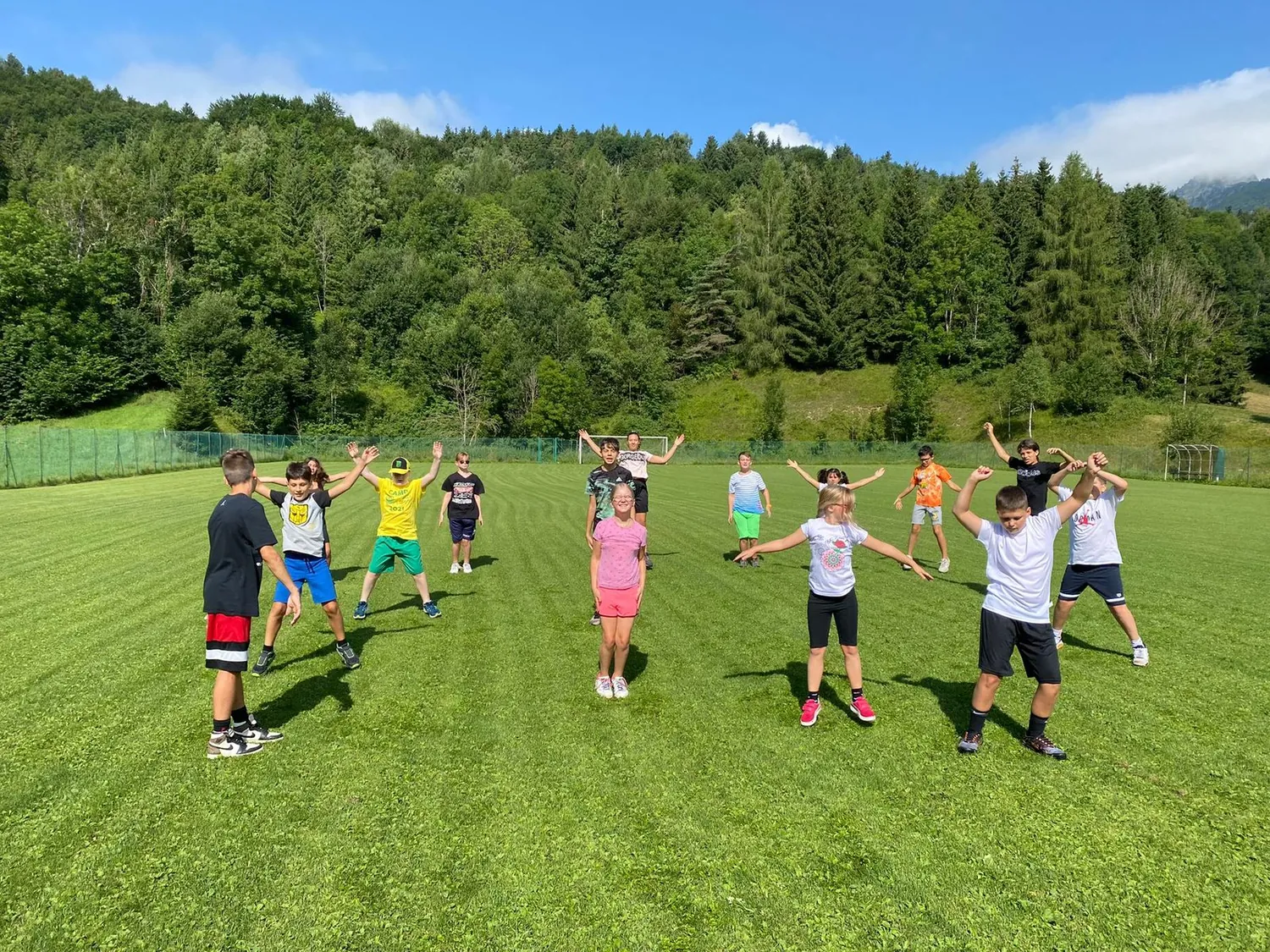 Gruppo di bambini del camp a braccia aperte sul prato, le montagne sullo sfondo
