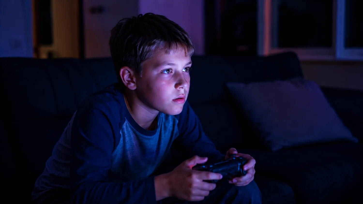 Un bambino al buio gioca ai videogiochi con il controller, il volto illuminato dallo schermo